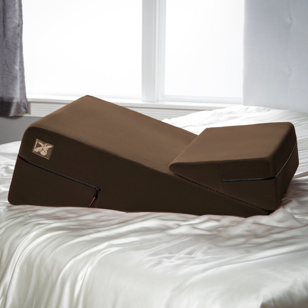 Brown wedge-shaped lounging cushion with zippered pocket and small rectangular logo patch