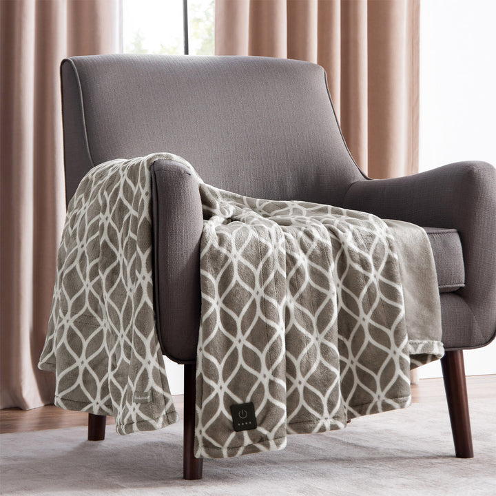 Taupe heated plush throw with white trellis pattern draped over a gray armchair.