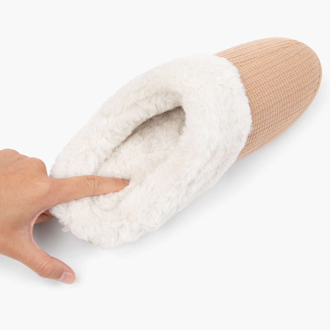 Beige slipper with white fur lining held by a hand on a white background