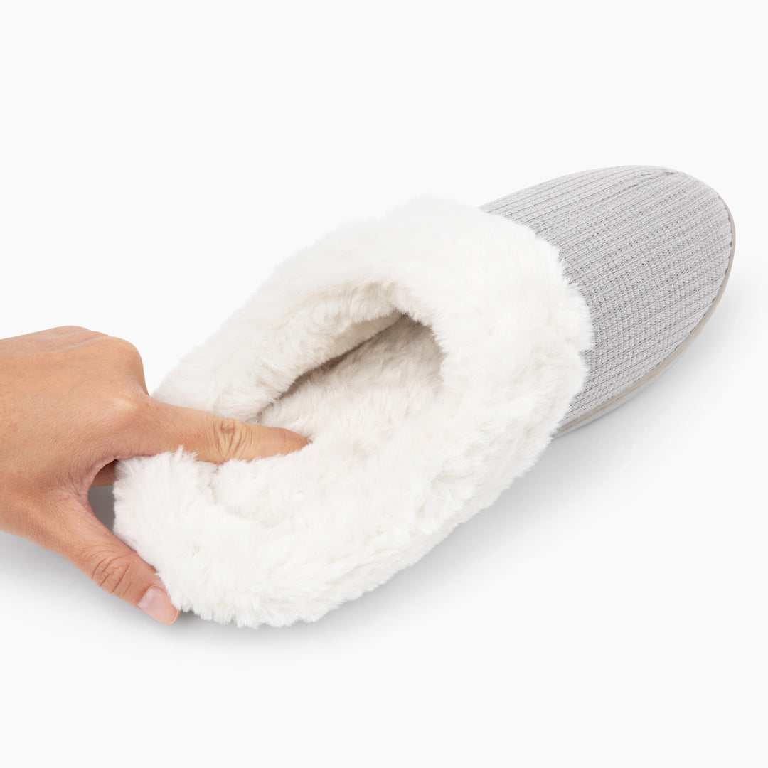 Gray slipper with white fur lining held by a hand on a white background