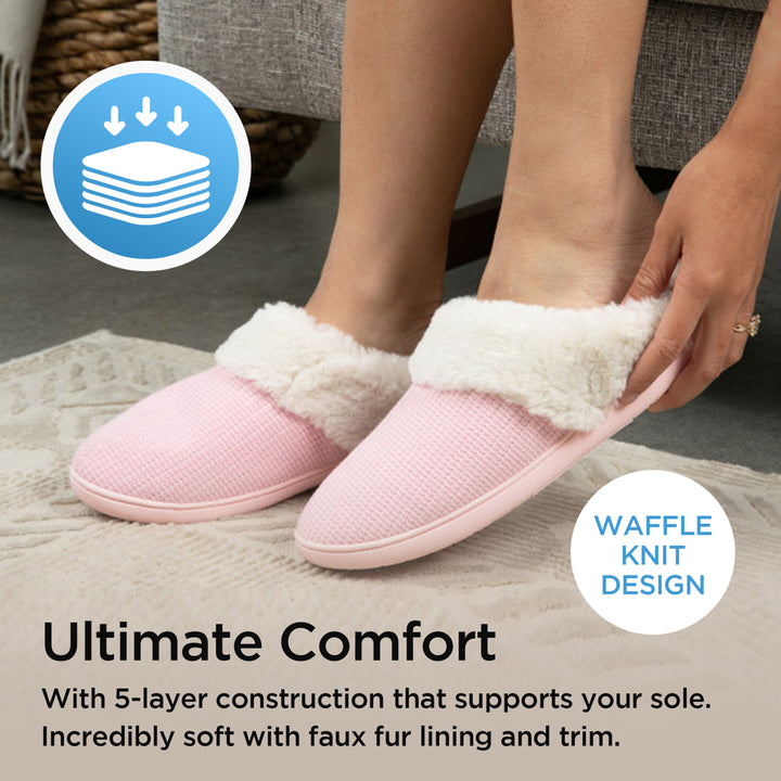 Pink slippers with white fur lining worn by a person, on a soft surface.