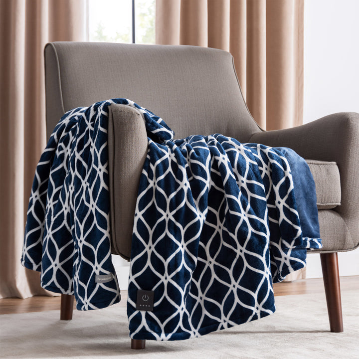 Navy blue and white patterned blanket draped over a gray armchair with beige curtains in the background.