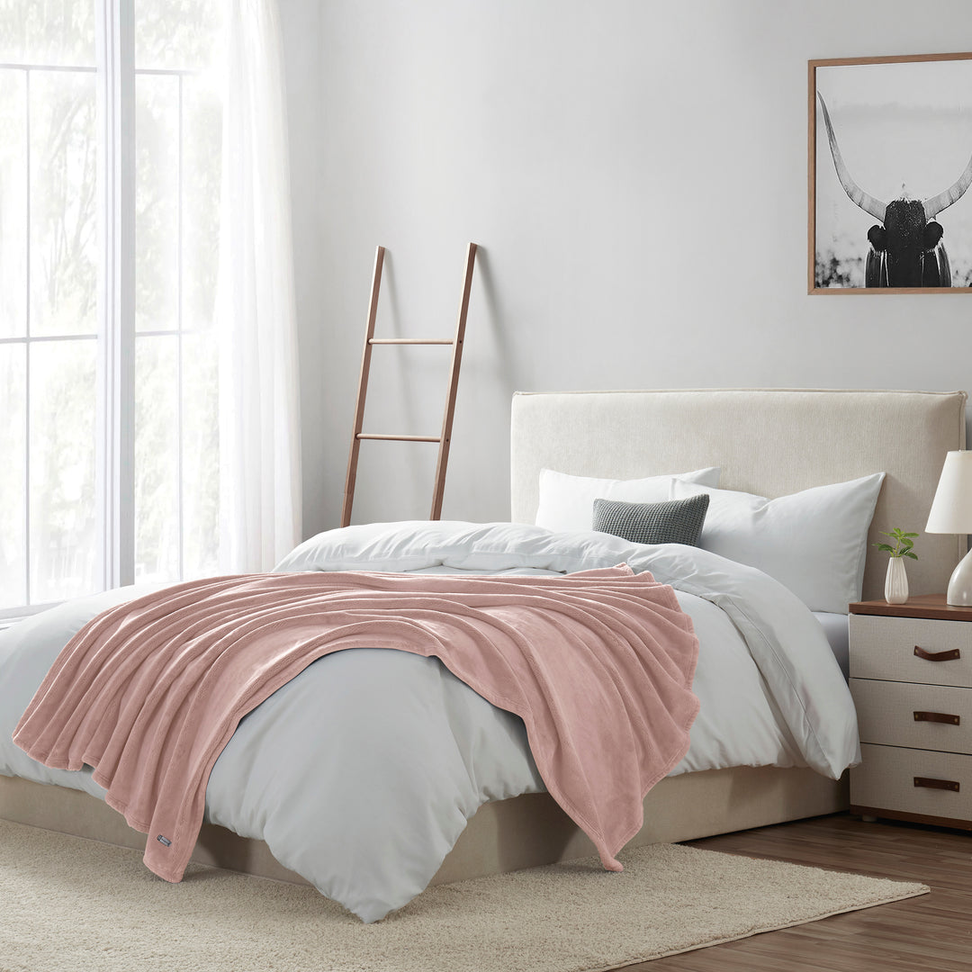 Bedroom with a bed featuring a pink blanket, white bedding, and a nightstand with a lamp.