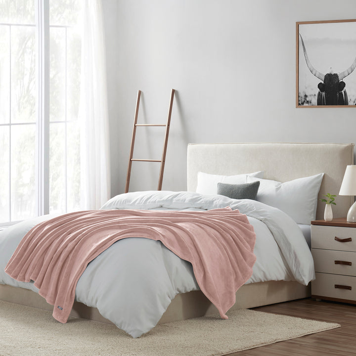Bedroom with a bed featuring a pink blanket, white bedding, and a nightstand with a lamp.