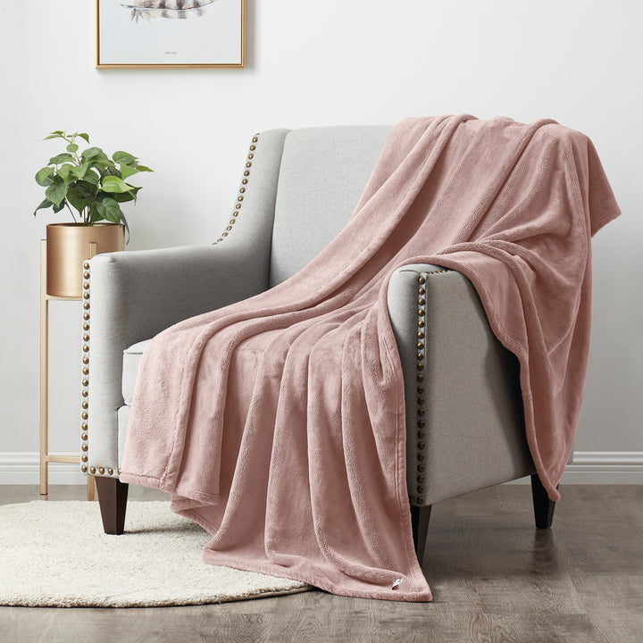 Pink blanket draped over a gray armchair in a room with a plant and gold side table.