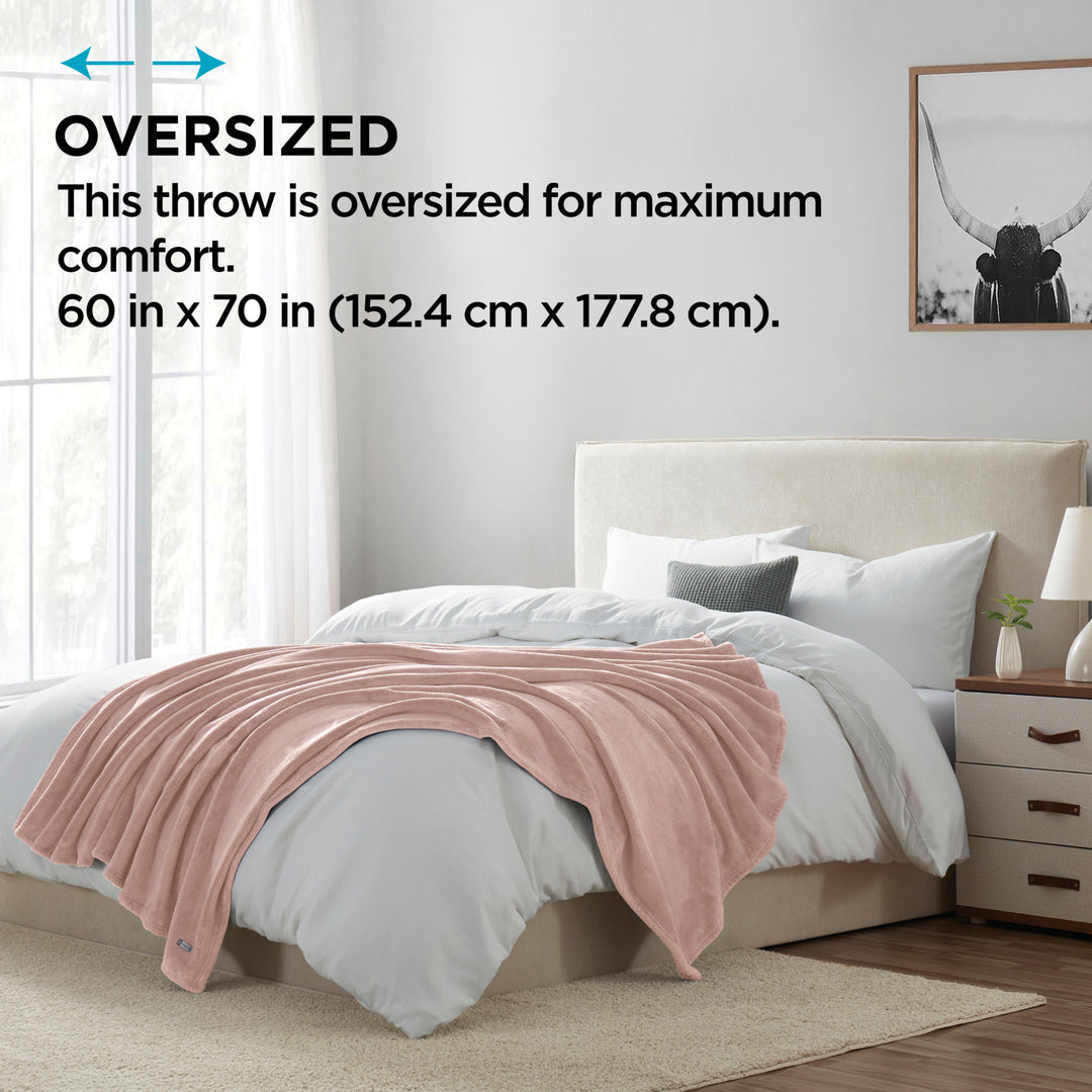 Pink throw blanket on a bed in a bedroom with text indicating oversized size.