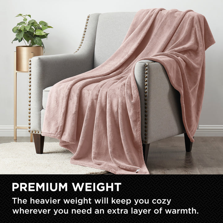 Pink blanket draped over a gray armchair in a living room setting with text about premium weight.