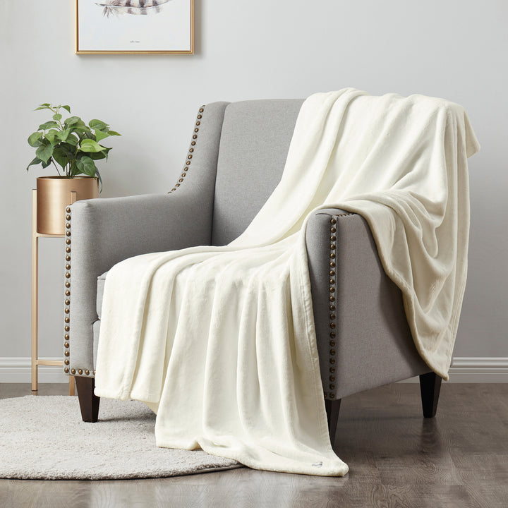 White blanket draped over a gray armchair in a room with a plant and framed picture on the wall.