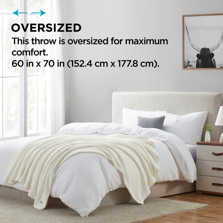 Oversized throw blanket draped over a bed in a bedroom setting with text indicating size.