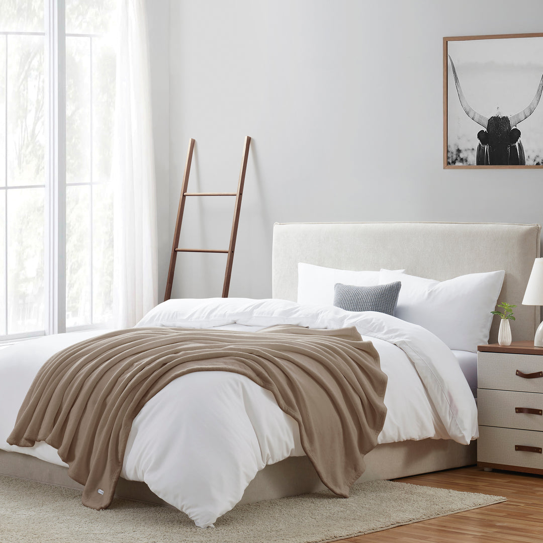 Neatly made bed with beige blanket in a bright bedroom