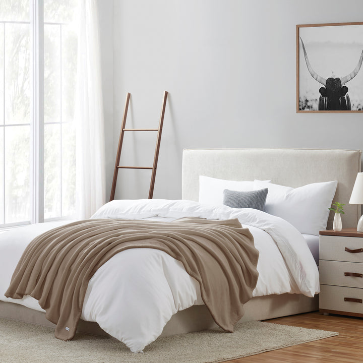 Neatly made bed with beige blanket in a bright bedroom
