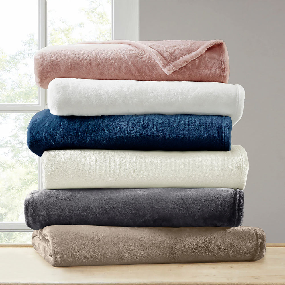 Stack of folded blankets in various colors on a wooden surface with a window in the background.