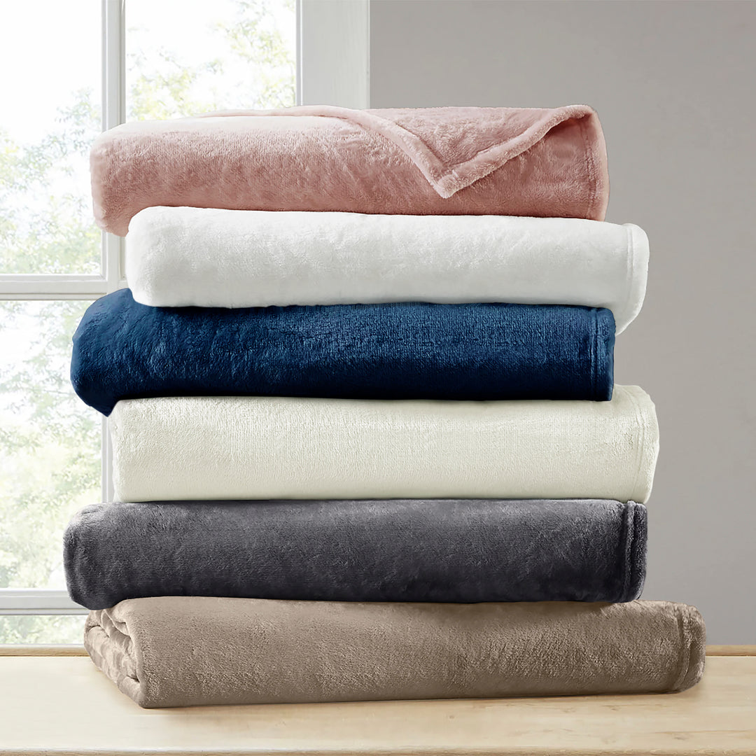 Stack of folded blankets in various colors on a wooden surface with a window in the background.