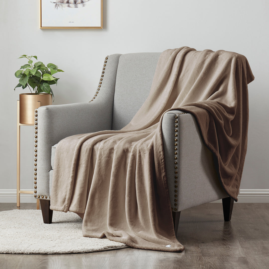 Beige blanket draped over a gray armchair in a room with a plant and framed picture on the wall.