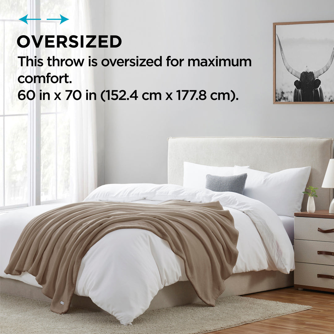 Beige throw blanket on a bed in a bedroom with text indicating oversized size.