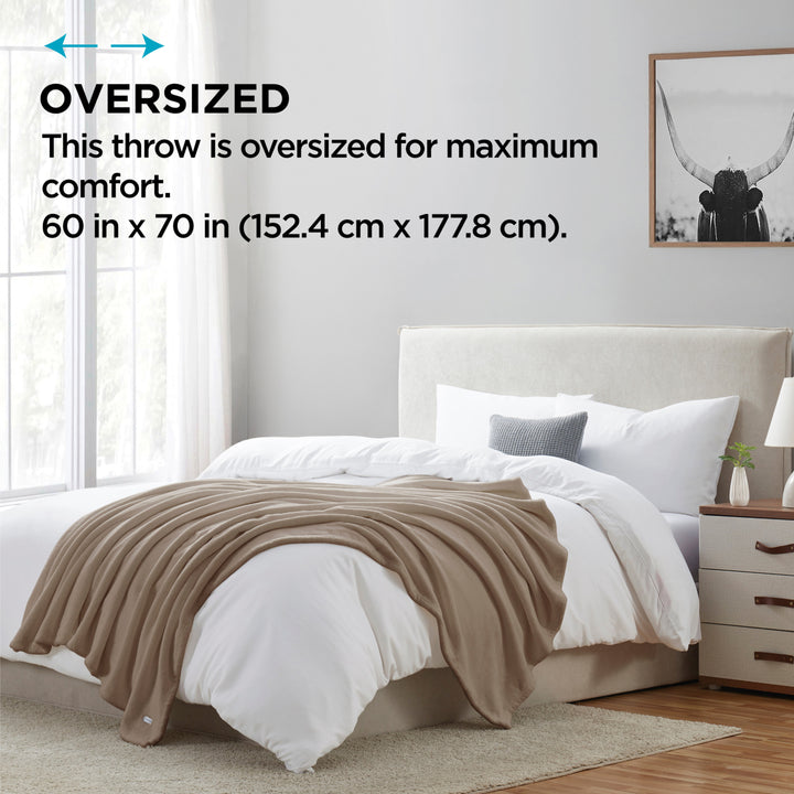 Beige throw blanket on a bed in a bedroom with text indicating oversized size.