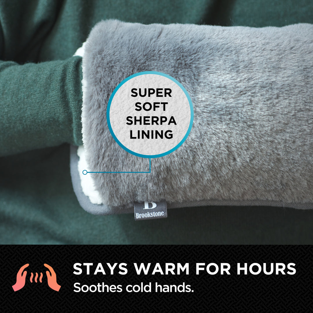 Close-up of a person using the Brookstone Snuggly Hand Warmer in charcoal gray, showing the super-soft Sherpa lining and highlighting that it stays warm for hours to soothe cold hands.