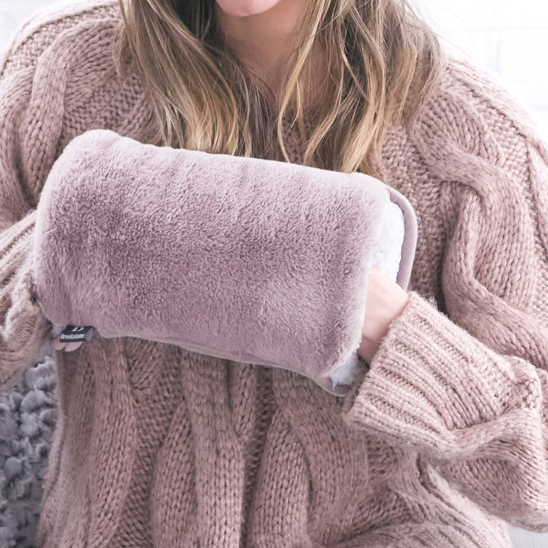 Person wearing a cozy pink sweater holding a fluffy pink pillow.