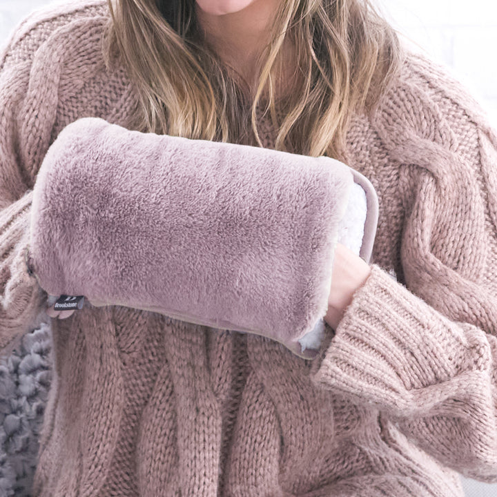 Person wearing a cozy pink sweater holding a fluffy pink pillow.