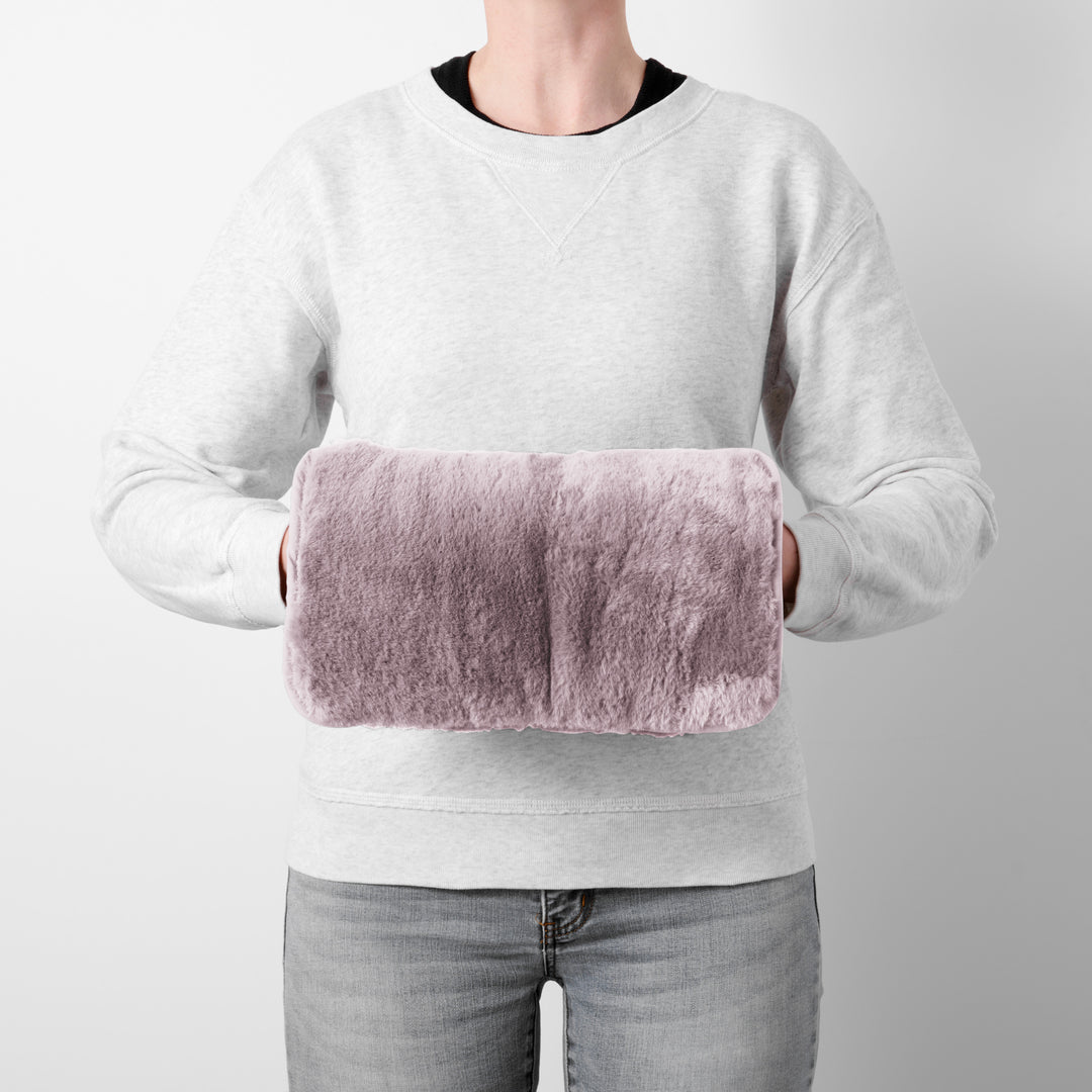 Person holding a pink heating pad against their chest on a plain background