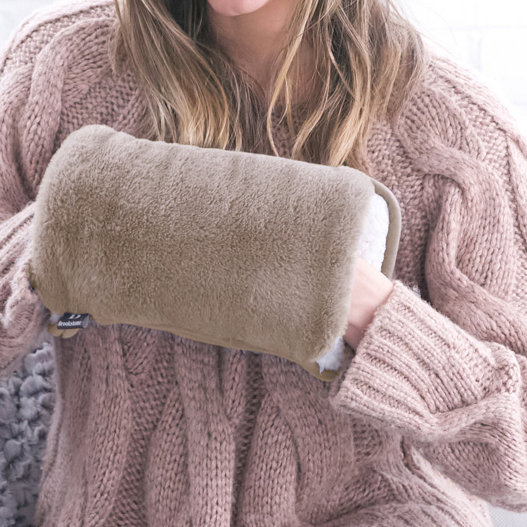 Person holding a beige plush pillow wearing a pink knitted sweater.