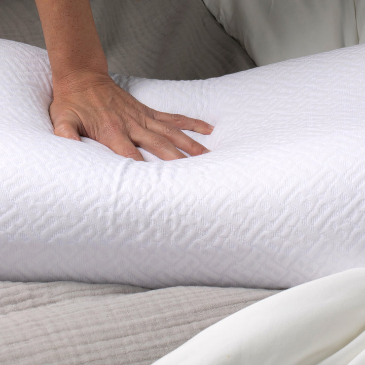 Hand pressing into a white pillow on a bed with beige bedding.
