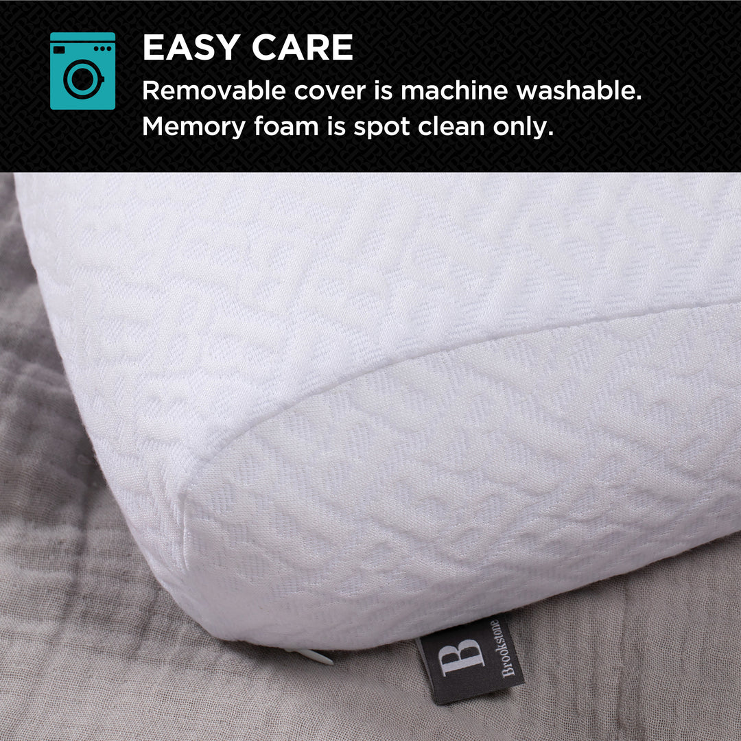 Close-up of a white textured memory foam pillow on a bed, showing the removable washable cover and Brookstone tag.