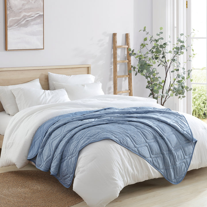 Bed with white bedding and a blue throw blanket in a bright bedroom.