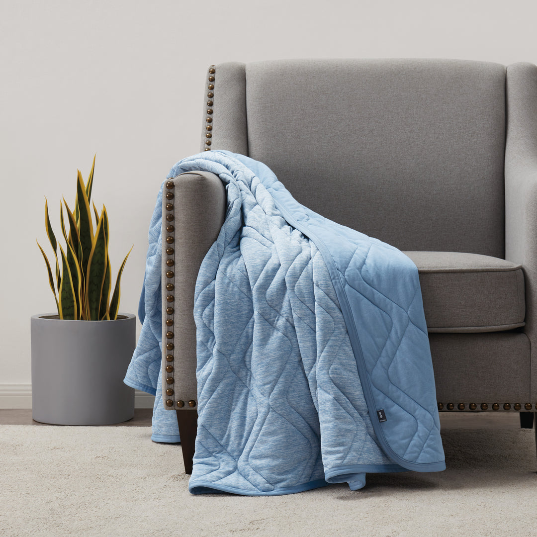 Blue quilted blanket draped over a gray armchair in a room with a plant.