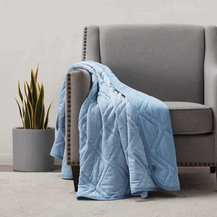 Blue quilted blanket draped over a gray armchair in a room with a plant.