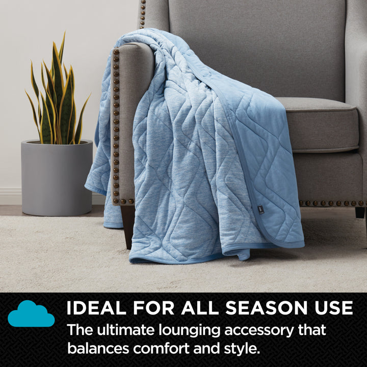Blue quilted blanket draped over a gray armchair with a plant in the background.