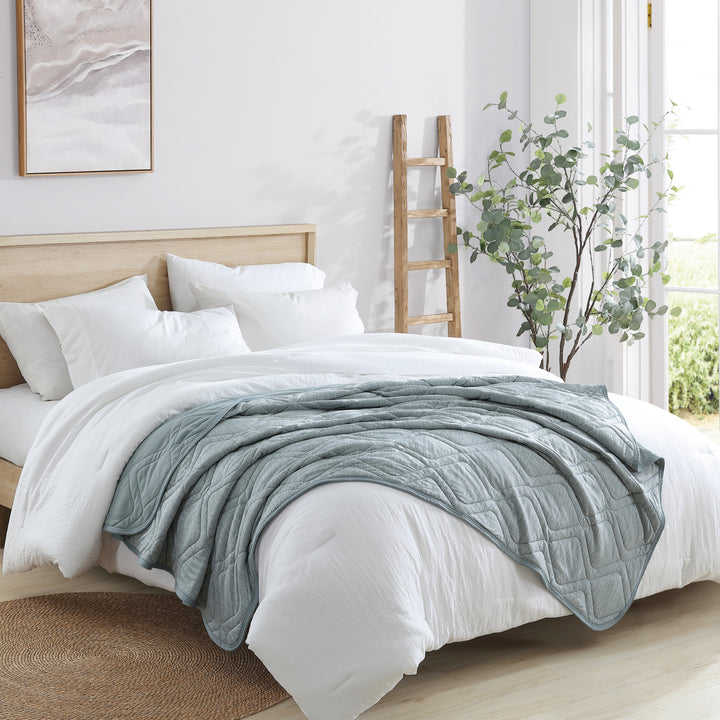 Bed with white bedding and a light blue comforter in a bright bedroom.