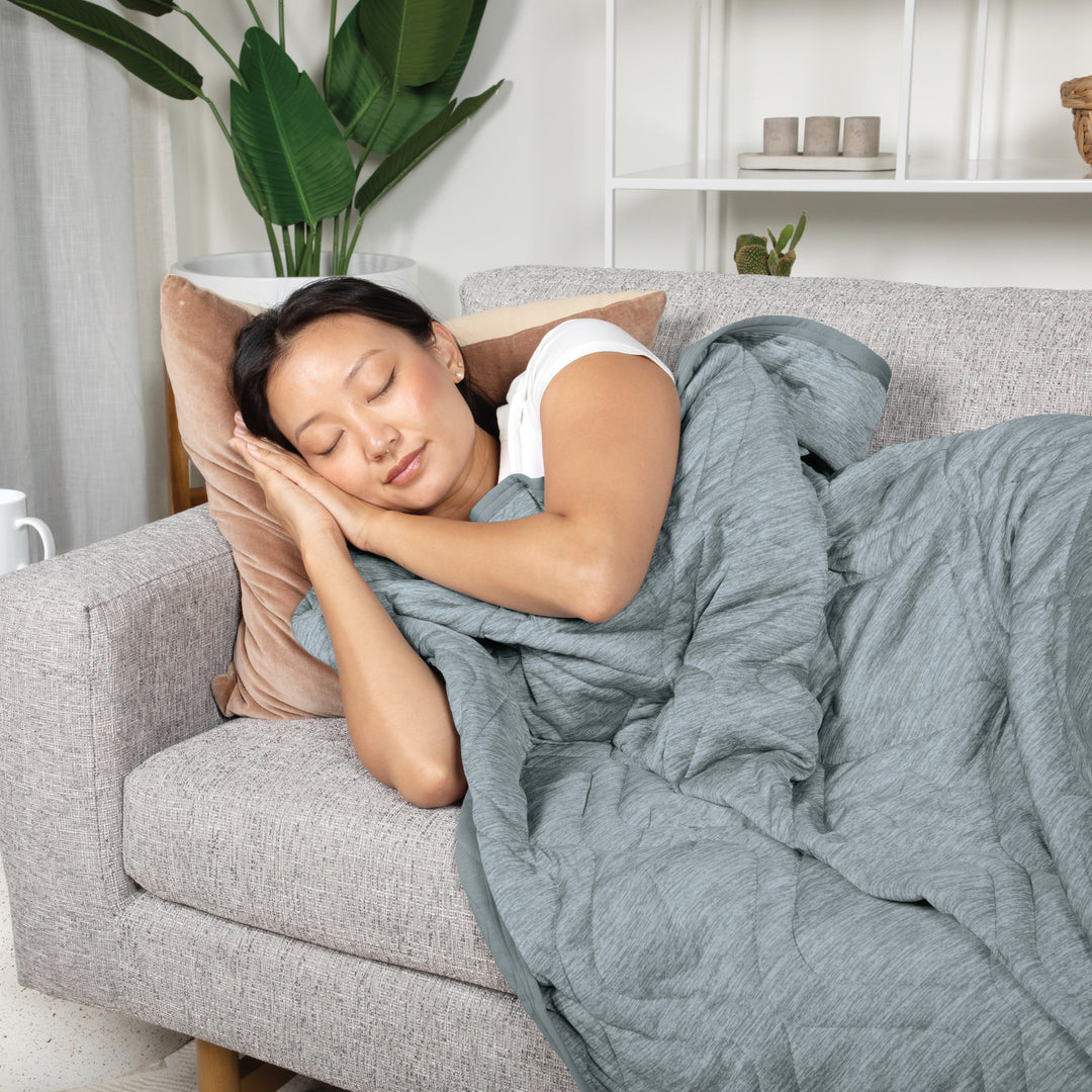 Woman sleeping on a couch with a gray blanket in a cozy living room.