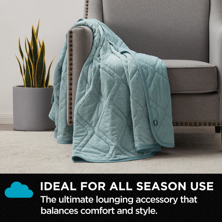Light blue quilted blanket draped over a gray armchair with a plant in the background.