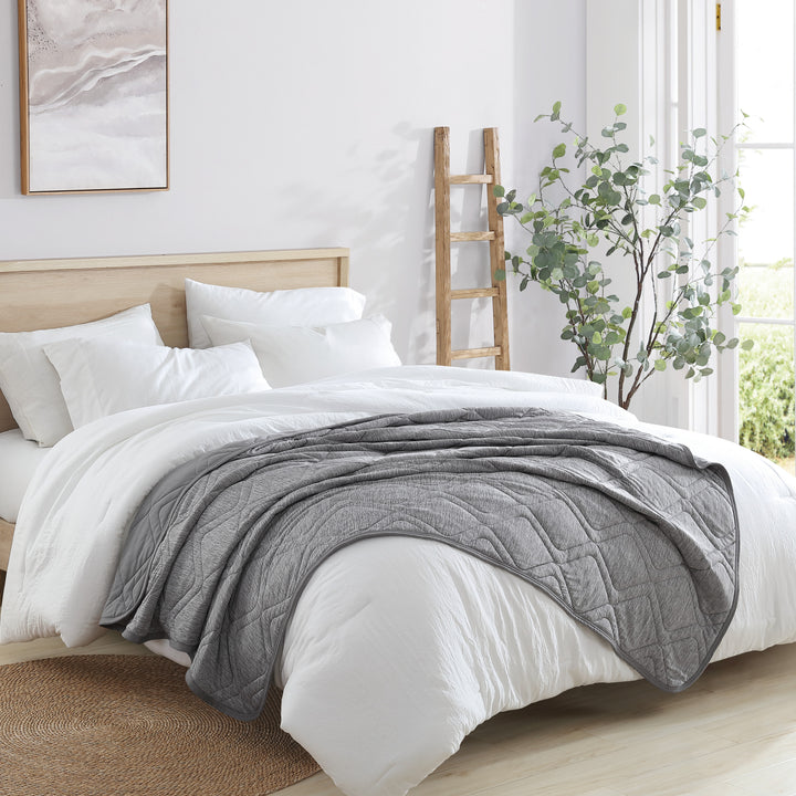Bed with white bedding and a gray comforter in a bright bedroom.