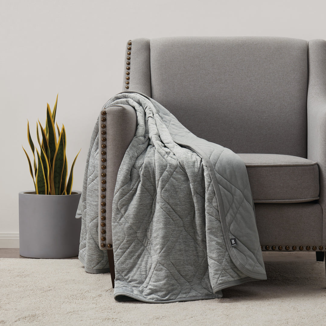 Gray quilt draped over a gray sofa in a living room setting with a plant in the background.