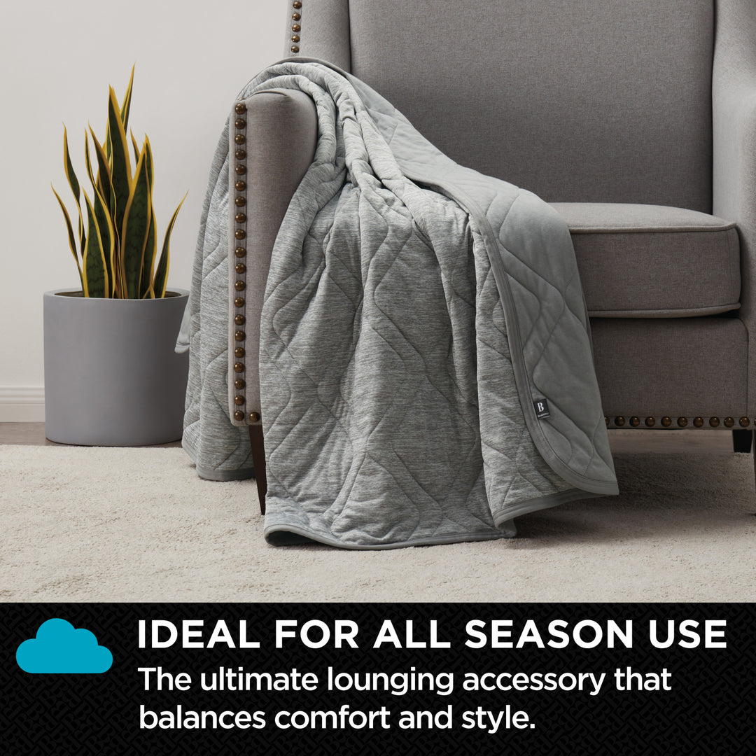 Gray quilted blanket draped over a gray armchair with a plant in the background.