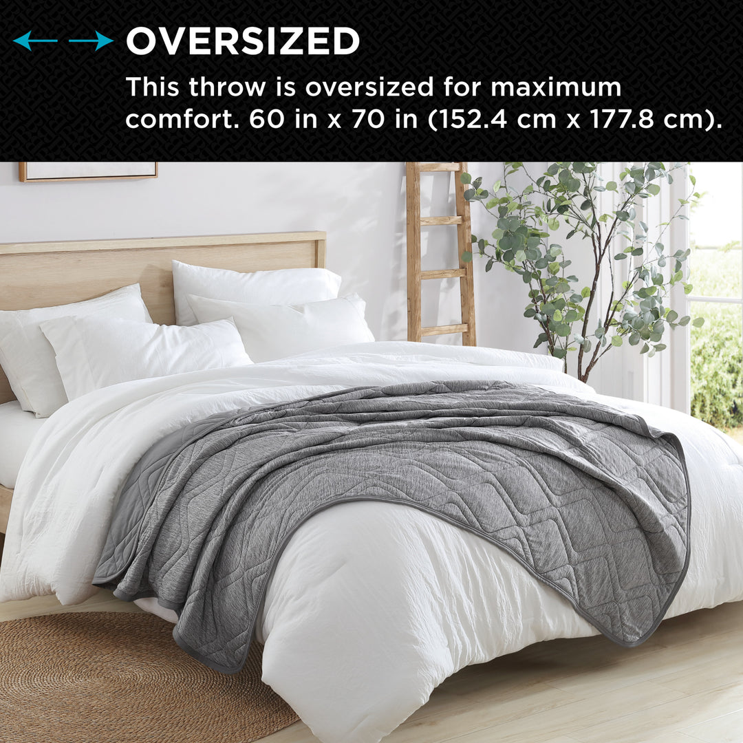 Gray throw blanket on a bed with text indicating oversized size and comfort.