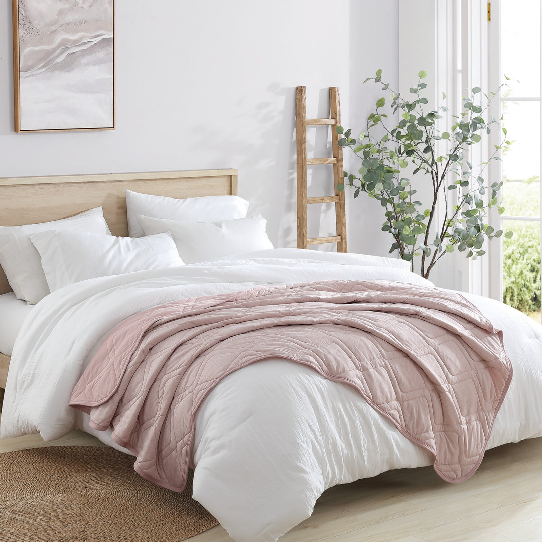 Bedroom with a bed featuring white bedding and a pink blanket, wooden ladder, and plant.