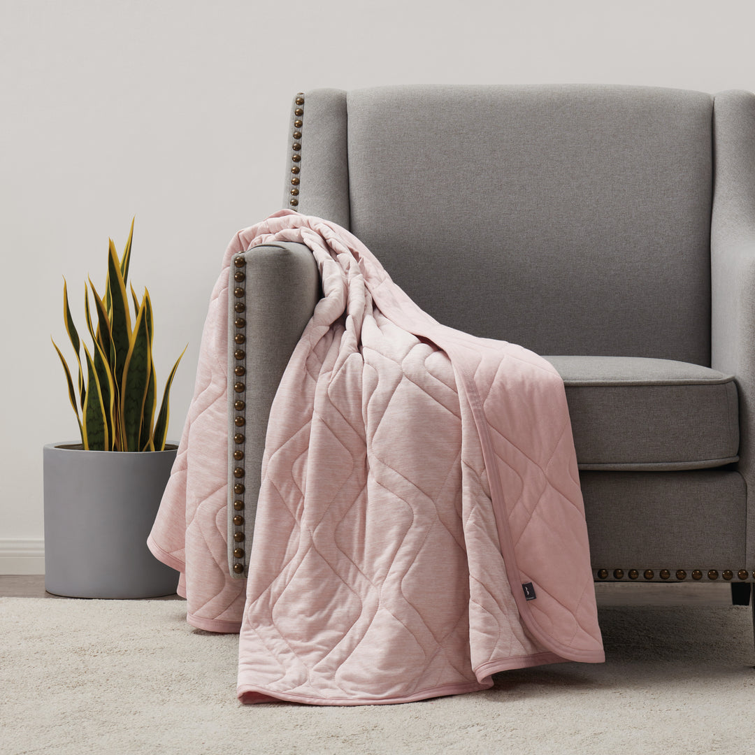 Pink quilt draped over a gray armchair in a room with a plant.