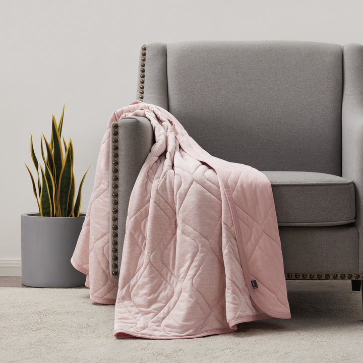 Pink quilt draped over a gray armchair in a room with a plant.