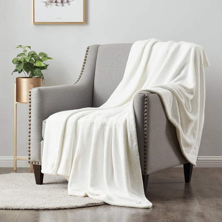 White blanket draped over a gray armchair in a room with a plant and framed picture on the wall.