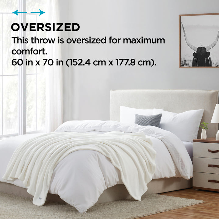 White oversized throw blanket draped over a bed in a bedroom setting.