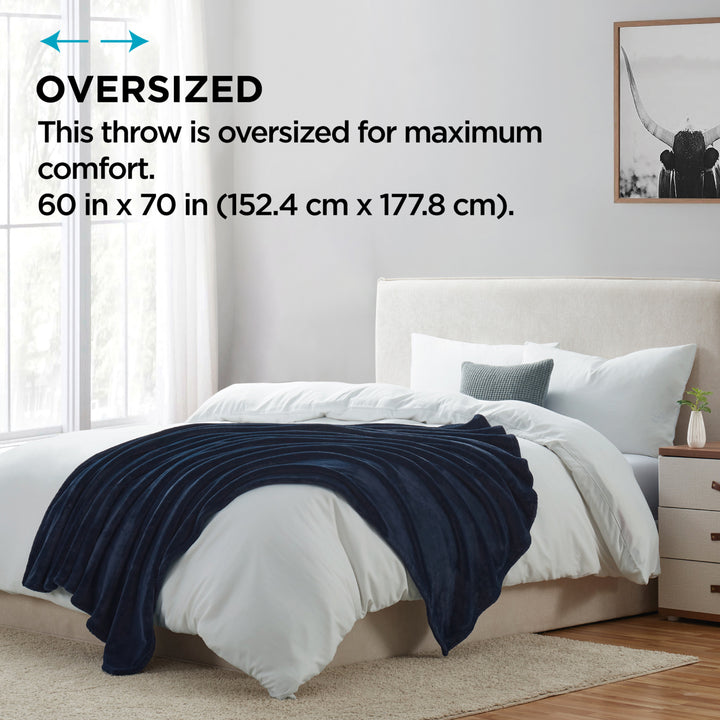 Oversized navy plush throw blanket displayed on a bed, highlighting its large 60 in x 70 in size for maximum comfort.