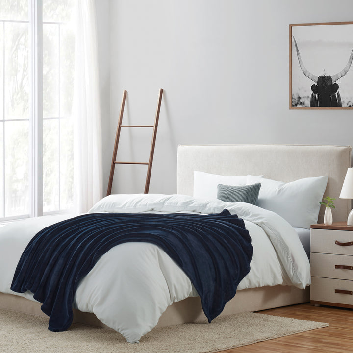 Bedroom with a bed featuring a navy blanket, white bedding, and a nightstand.