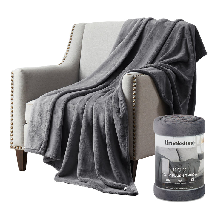 Plush Silver throw blanket draped over a grey armchair next to the rolled Brookstone Nap Cozy Plush Throw packaging.