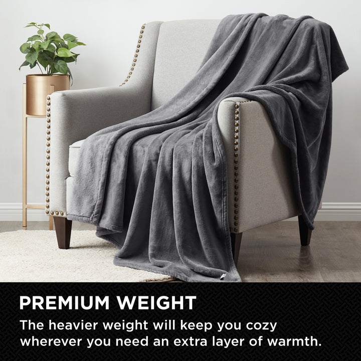 Lifestyle image of the plush throw silver blanket draped over an armchair with graphic text highlighting its premium, heavier weight for added warmth.