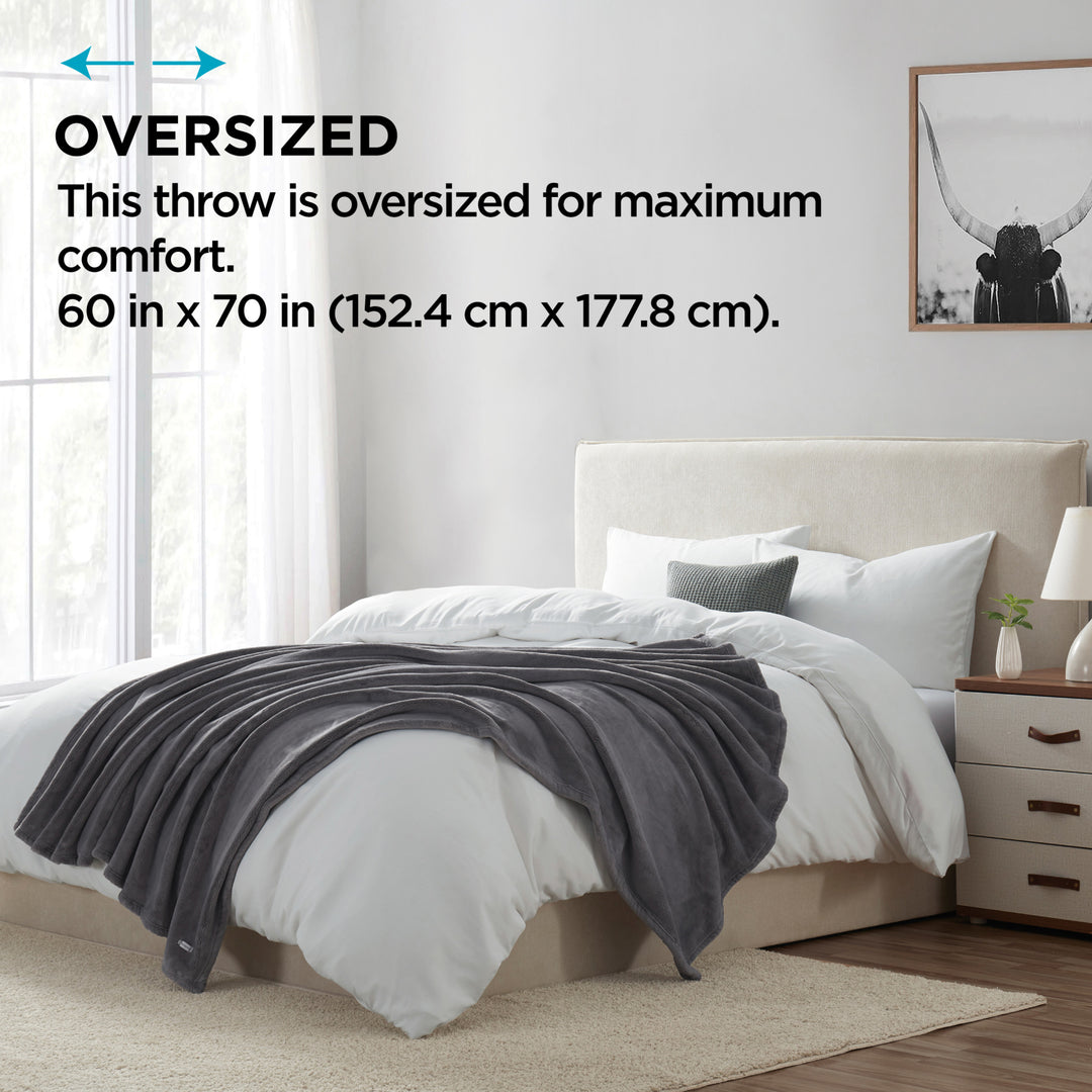 Oversized gray plush throw blanket displayed on a bed, highlighting its large 60 in x 70 in size for maximum comfort.