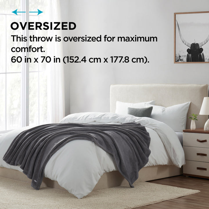 Oversized gray plush throw blanket displayed on a bed, highlighting its large 60 in x 70 in size for maximum comfort.