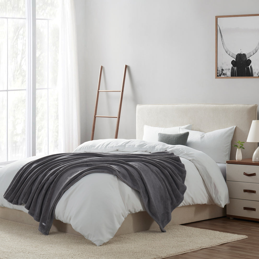 Gray plush throw blanket styled on a neatly made bed in a modern bedroom setting.